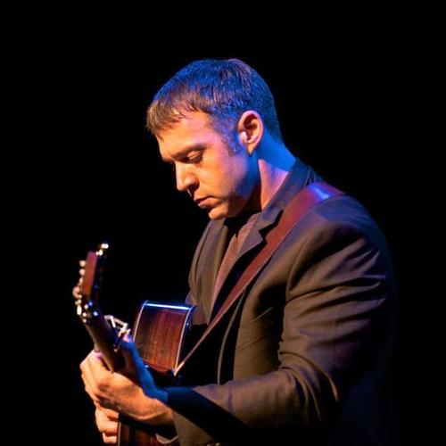 Sam Pacetti playing acoustic guitar under blue stage light